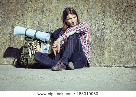 Man tourist backpacker relaxing outdoor sitting tired by grunge wall. Adventure summer tourism active lifestyle. Young hipster guy tramping