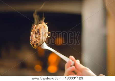 Smoky barbeque pork meat on the fork. Meat on the coals with blurred bonfire background.
