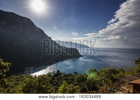 sun shining above mountains with blue sea in bay of mediterranean sea