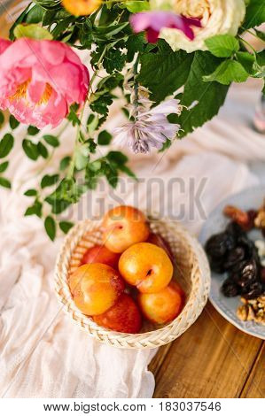 picnic, food, summer, holiday concept - close-up on the festively decorated table with beautiful pink peony and white rose flowers, fresh and dried fruits, nectarines, walnuts, prunes, tableware