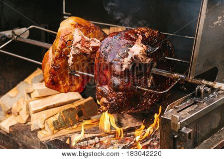 Large chunks of delicious pork hams cooked on an open fire. The street food. Food outdoors. Camping and cooking on a spit over the fire. Camping.