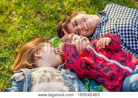 Mom and two kids lie on the grass in the park, laugh, spring, family