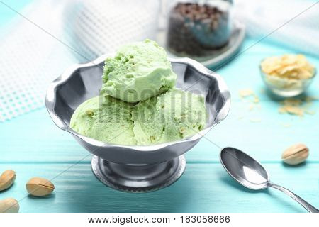 Tasty pistachio ice cream in bowl and nuts on wooden table