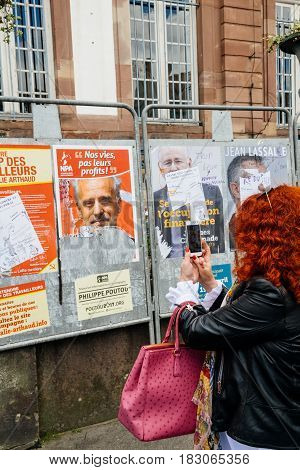 STRASBOURG FRANCE - APR 23 2017: Woman taking on mobile phone Presidential campaign posters of candidates fro French presidency