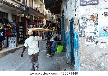 Zanzibar, Tanzania - July 14, 2016: Local market in Tanzania, muslim man selling colorful glasses, old and half-ruined buildings around