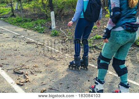 Two girls ride on rollers on a very bad road. The fallen branches lie on the asphalt. Sport Difficulties. Extreme rollerskating.