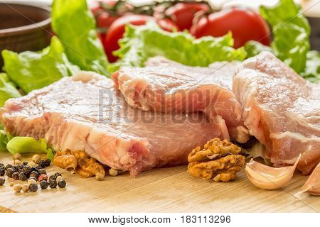 Slices of raw meat. Pork escalope on a wooden board. With the ingredients for cooking.