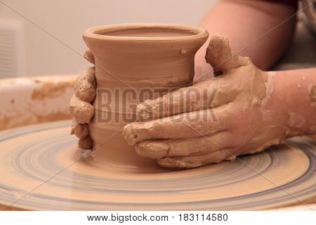 hands of a potter, creating an earthen jar on a pottery wheel