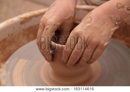 hands of a potter, creating an earthen jar on a pottery wheel