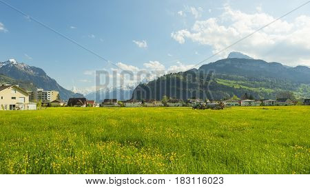 Panorama of the town Brunnen. Traditional Alpine meadows with luscious bright grass. Tractor fertilizes the field. Travel to Europe.