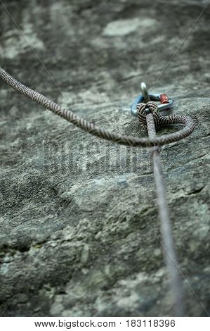 cliff and rope fixed on the quickdraw. Black safety rope fixed on climbing quickdraw fixed on the jumper, on a background of yellow rocks in sunny weather