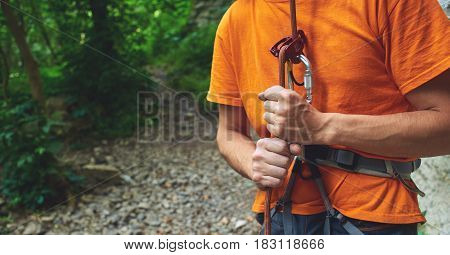 A man insures climber through a belay device. Tubular device on locking carabiner. hands and belay device close up