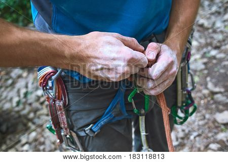 A man climber Untying the knot on a climbing harness. hands in chalk close up
