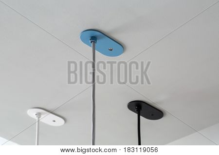 Three multicolored bracing with hanging cables on the light ceiling. They are white, blue and black colored. Closeup photo. Horizontal.