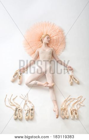 A young ballerina in white leotard is lying on the floor. The model closed her eyes. In the hands of a dancer, ribbons of pawns. Studio shoting, topshot.