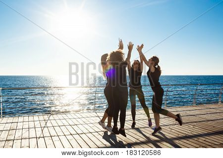 Silhouettes of young beautiful sportive girls giving highfive near sea at sunrise.