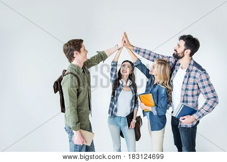 Four Young Students In Casual Clothes Holding Books And Giving Highfive On White