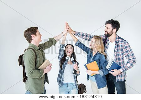 Four Young Students In Casual Clothes Holding Books And Giving Highfive On White