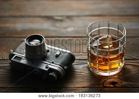 Glass of whiskey and vintage old 35mm rangefinder camera on wooden background
