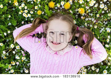 Child on green grass lawn with daisy and dandelion flowers on sunny summer day. Kid playing in garden. Little girl dreaming and relaxing. Kids on Easter egg hunt in spring park. Children gardening.
