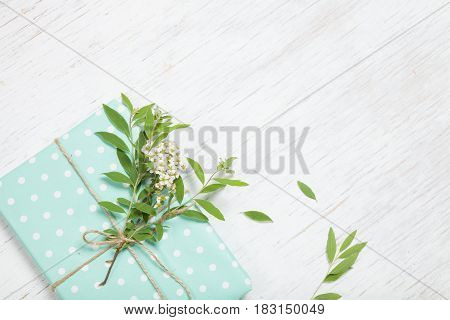 Top view on decorated birthday gift with garden tree branch and flowers. Packing present for the party. Wrapping gift with flower decor and turquoise paper. Holidays concept. Flat lay.