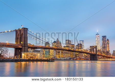 Brooklyn bridge and New York City Manhattan downtown skyline at dusk with skyscrapers illuminated over East River panorama. Panoramic composition.
