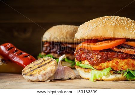 Two fresh tasty burger. Homemade hamburger with fresh vegetables close-up. Sesame buns with succulent beef patty grilled onions bacon tomato and fresh salad served on rustic wooden board.