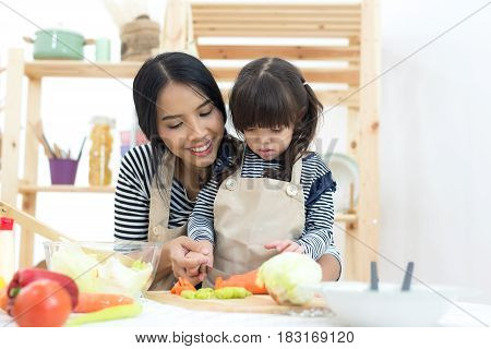 Mother and kid girl cooking and cutting vegetables on kitchen