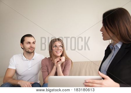 Smiling couple discussing future vacation with travel agent, man and woman planning real estate purchase consulting with broker, female agent explaining attractive mortgage offer to young happy family