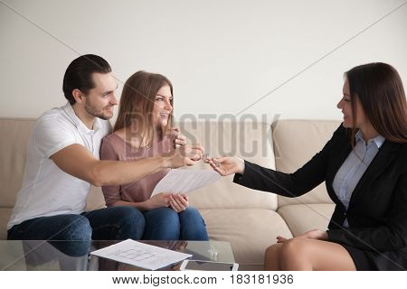 Female realtor giving keys to happy owners of apartment, couple of renters getting key of new home after signing rental agreement, young family starting new happy life in own house