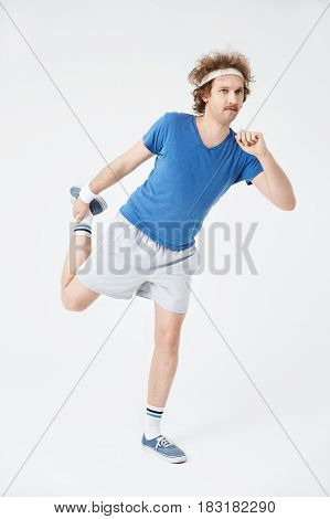 Full length portrait of young man stretching right leg holding foot with right hand