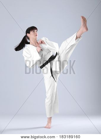 Young sporty woman practicing martial arts on light background