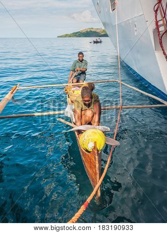 Hell-Ville Madagascar - December 19 2015: Malagasy vendors from their outrigger canoe offer fish and tropical fruits to ship passengers at Hell-Ville Nosy Be Island Madagascar.