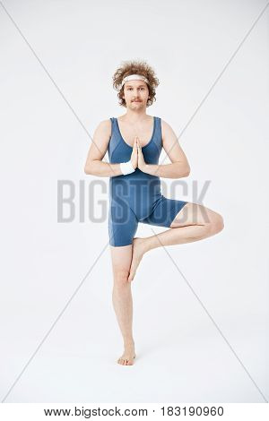 Yoga class. Out of date sport wear. Man practicing yoga, doing vrikshasana. Calm and quiet