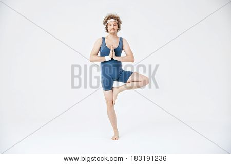 Man in old style sport clothing practicing yoga. Vrikshasana with eyes closed. Peace and harmony