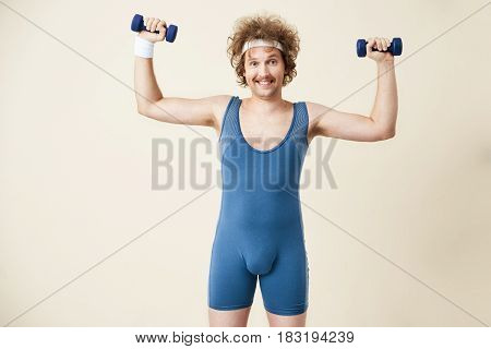 Closeup of young man in retro sport suit holding dumbbells in hands. Smiling at camera