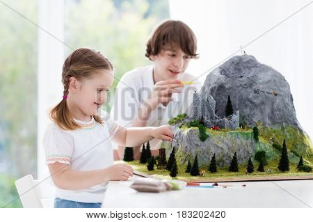 Children work on model building school project. Kids build miniature scale model mountain for geography class. Extracurricular activities and hobby club. Art and crafts for teenager and preschool.
