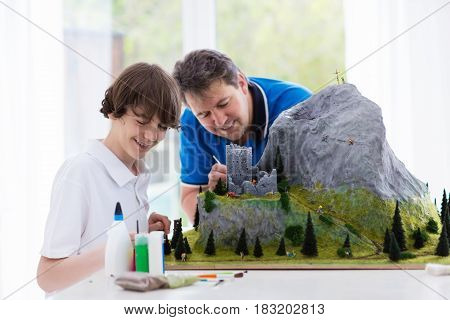 Father and son work on model building school project. Kids and parent build miniature scale model mountain for geography class. Extracurricular activities and family hobby. Art and crafts for child.
