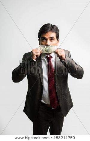 indian businessman holding indian currency note covering mouth or face and asking to keep silence or secret