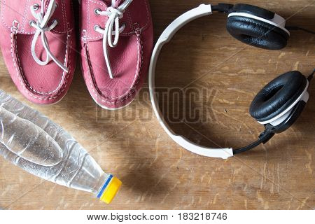 Pink sport shoes headphones bottle of water. Pair of sneakers on wooden background