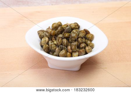 bowl with fresh capers on wooden table.