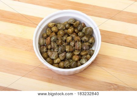 bowl with fresh capers on wooden table.