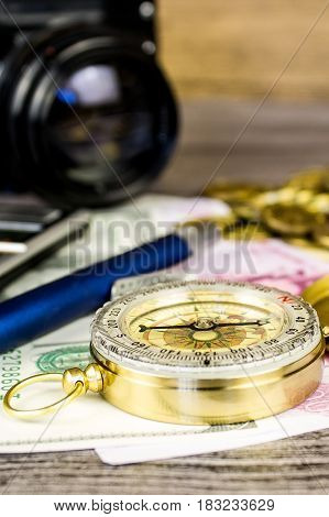 Composition of a tourist compass, banknotes, coins, calculator, pen and fotocamera on the gray wooden table