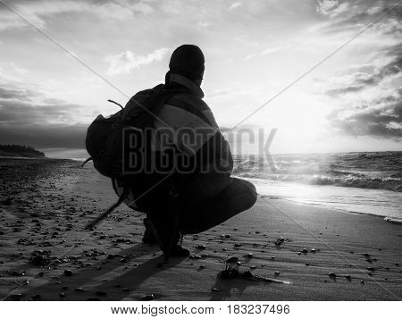 Man sit at evening sea. Hiker with backpack sit in squatting possition along beach. Vintage Style Toned effect