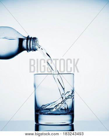 Water pouring into a wide glass from a bottle tinted in blue