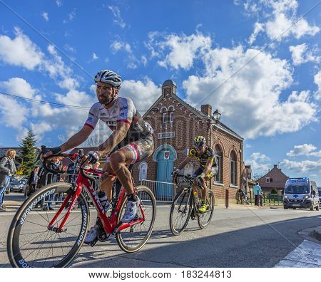 Louvil France - April 102016: Two cyclists riding in front of Louvil Town Hall in France during Paris Roubaix on 10 April 2016.