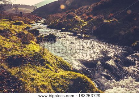 Retro Filtered Photo Of A Man Hiking In The Rugged Scottish Countryside Beside A Stream