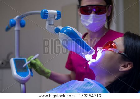 Close-up portrait of a female patient at dentist in the clinic. Teeth whitening procedure with ultraviolet light UV lamp.