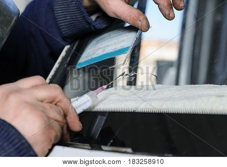 Repair cracked windshield. Fitter uses a syringe for applying the adhesive.