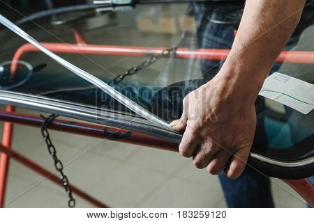 Car mechanic's hands are instilling decorative molding to seal of a windshield.